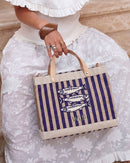 Person holding a striped tote bag with sardine beaded design and initials on a light background