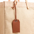 Dark brown leather gift tag with note on an Apolis bag, blank front
